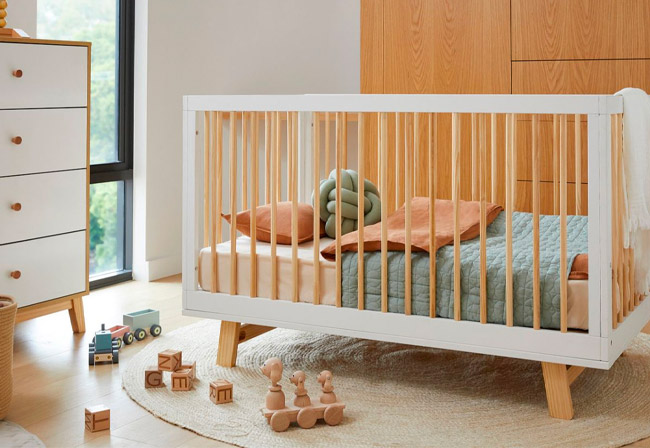 The bestselling Mocka Aspen Cot in a nursery next to a chest of drawers. 