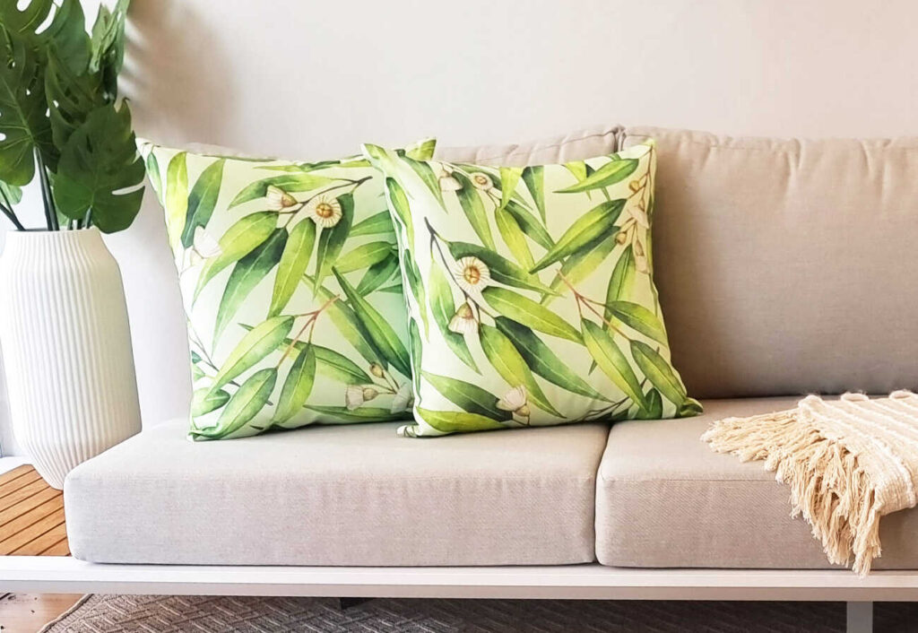 Two wattle-themed outdoor cushions on a beige sofa.