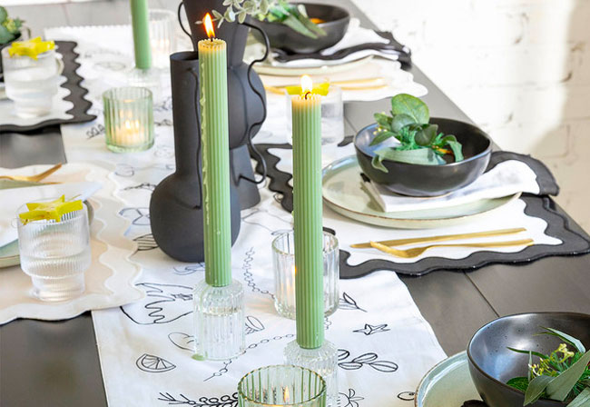 A dining table with green candles and black crockery.