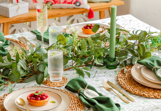 A Christmas table with green candles and a foliage garland.