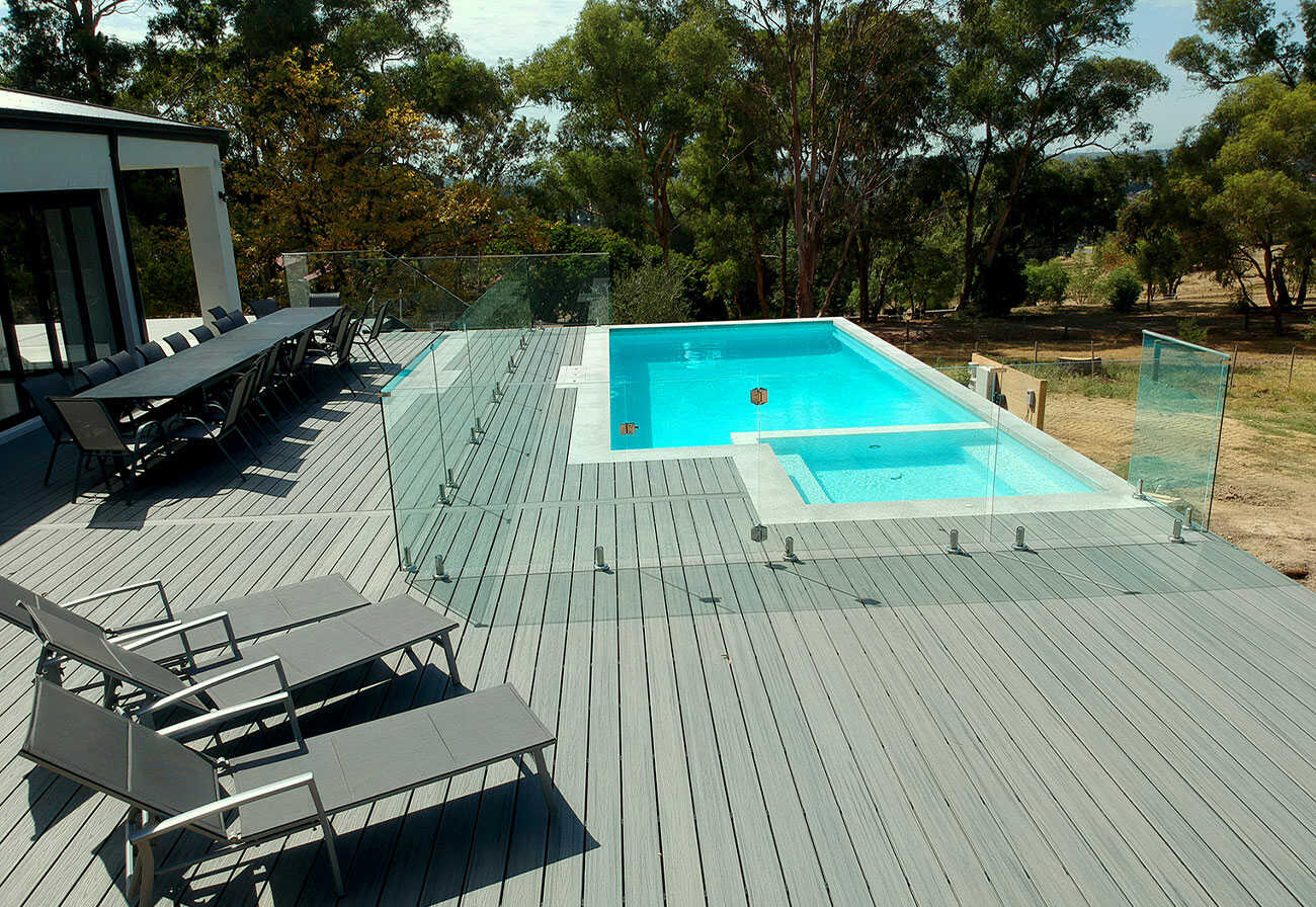 Backyard Australian swimming pool with a deck and glass fence.