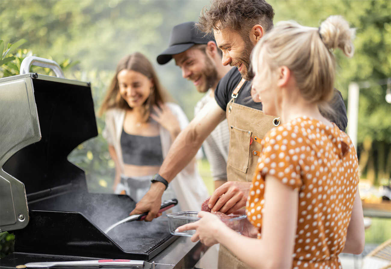 Group of people cooking around a bbq outdoors.