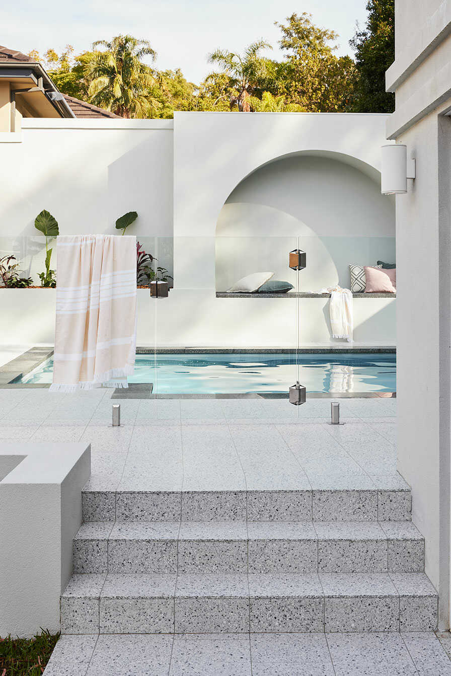 Steps up to a beautiful outdoor swimming pool with a glass fence.