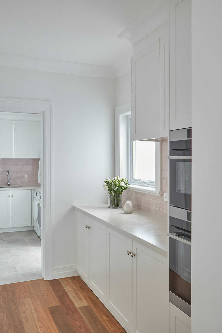 A modern kitchen and laundry with pale pink subway tiles.