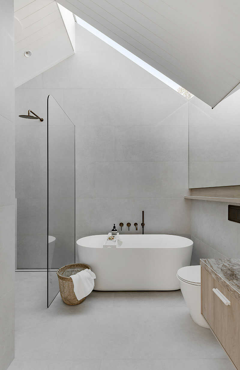 Modern bathroom fully tiled in grey with angled roof and freestanding bath.