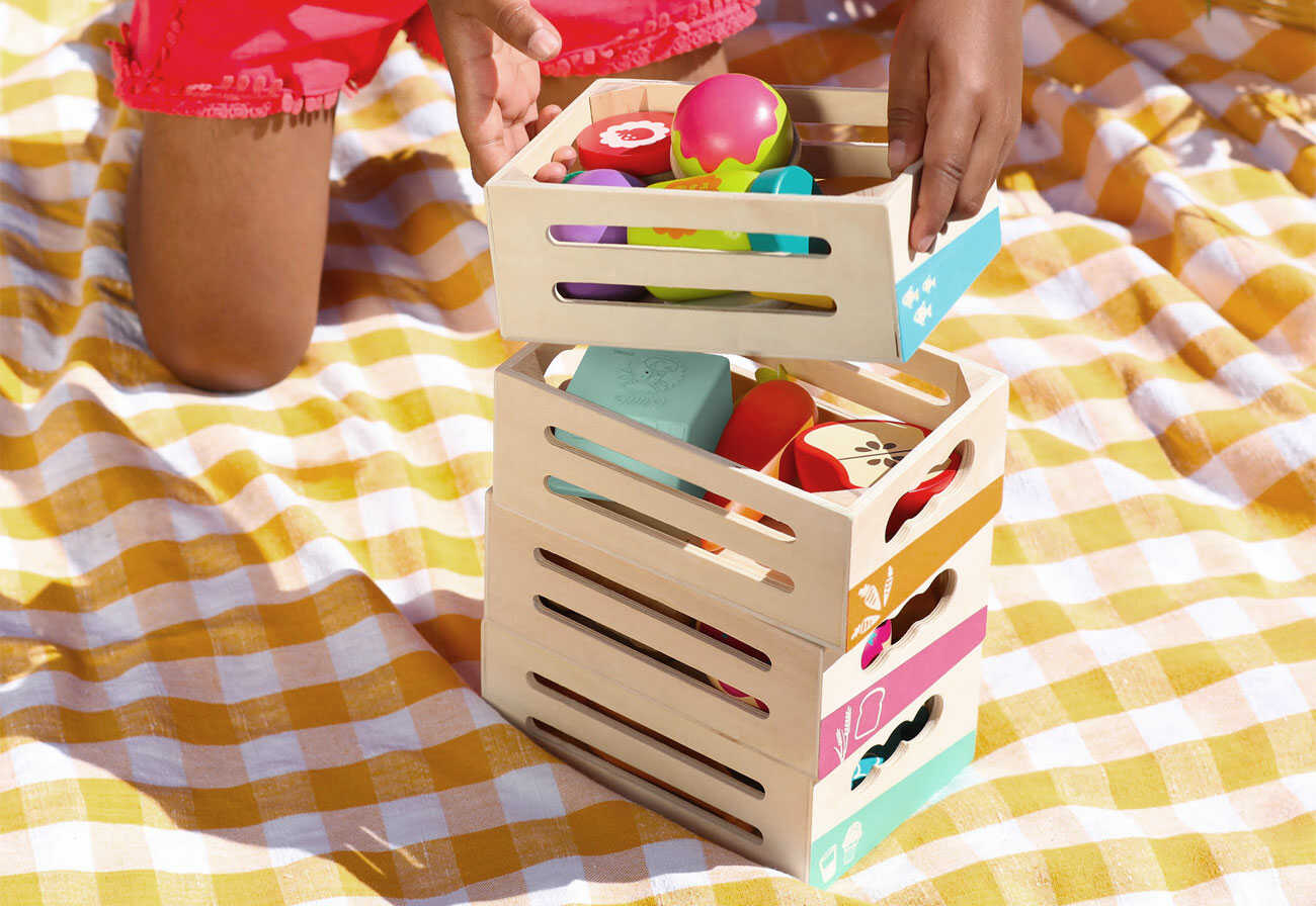 Child stacking crates of wooden play food.