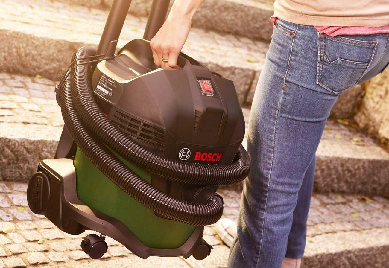 Person carrying a large vacuum cleaner up some outdoor steps.