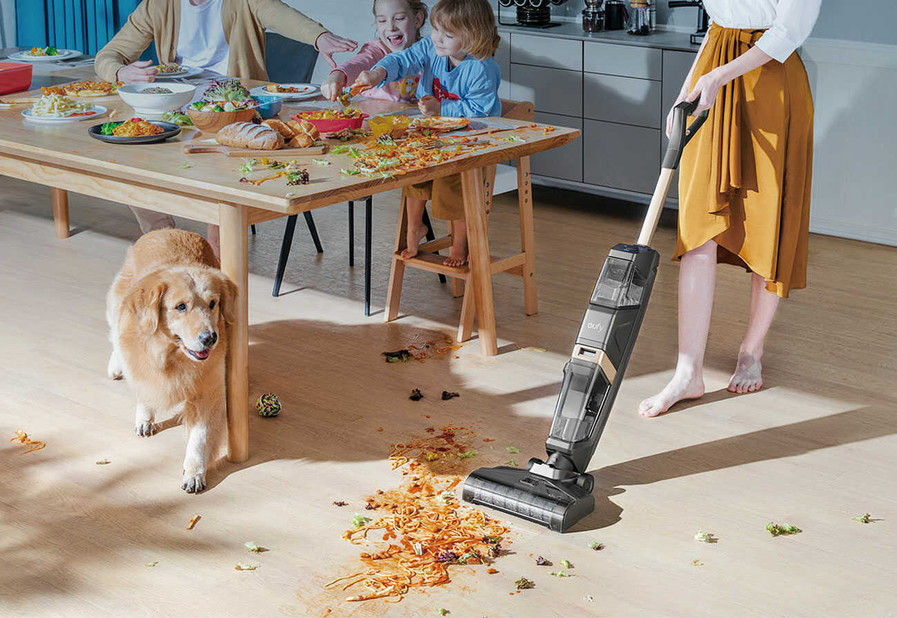 Woman vacuums spilled food next to a family dining table.