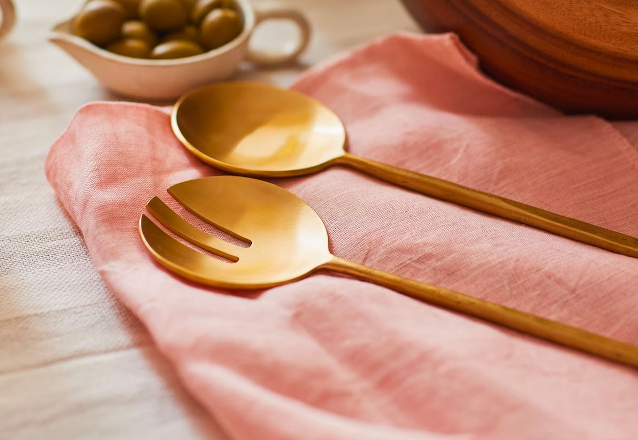 Brass serving utensils on a pink napkin.