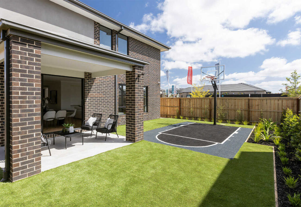 Backyard of a two-storey brick home with a sports surface and basketball ring.