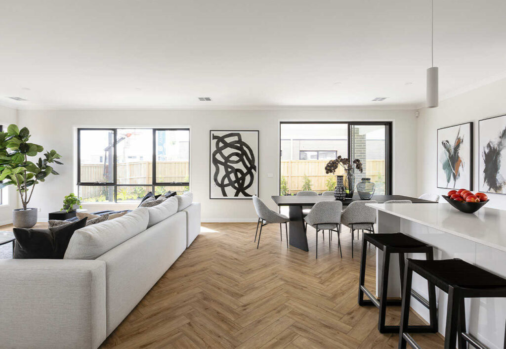 Modern kitchen, dining and living zone with a herringbone wood floor and neutral furnishings. 