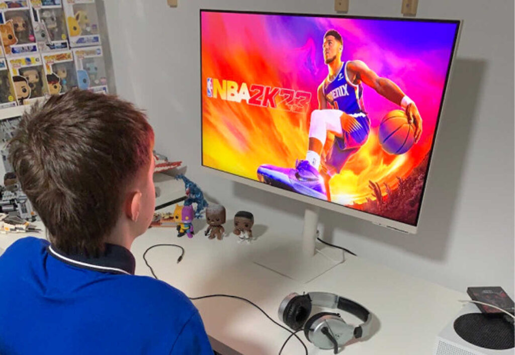 Boy sitting in front of a large monitor watching sport.