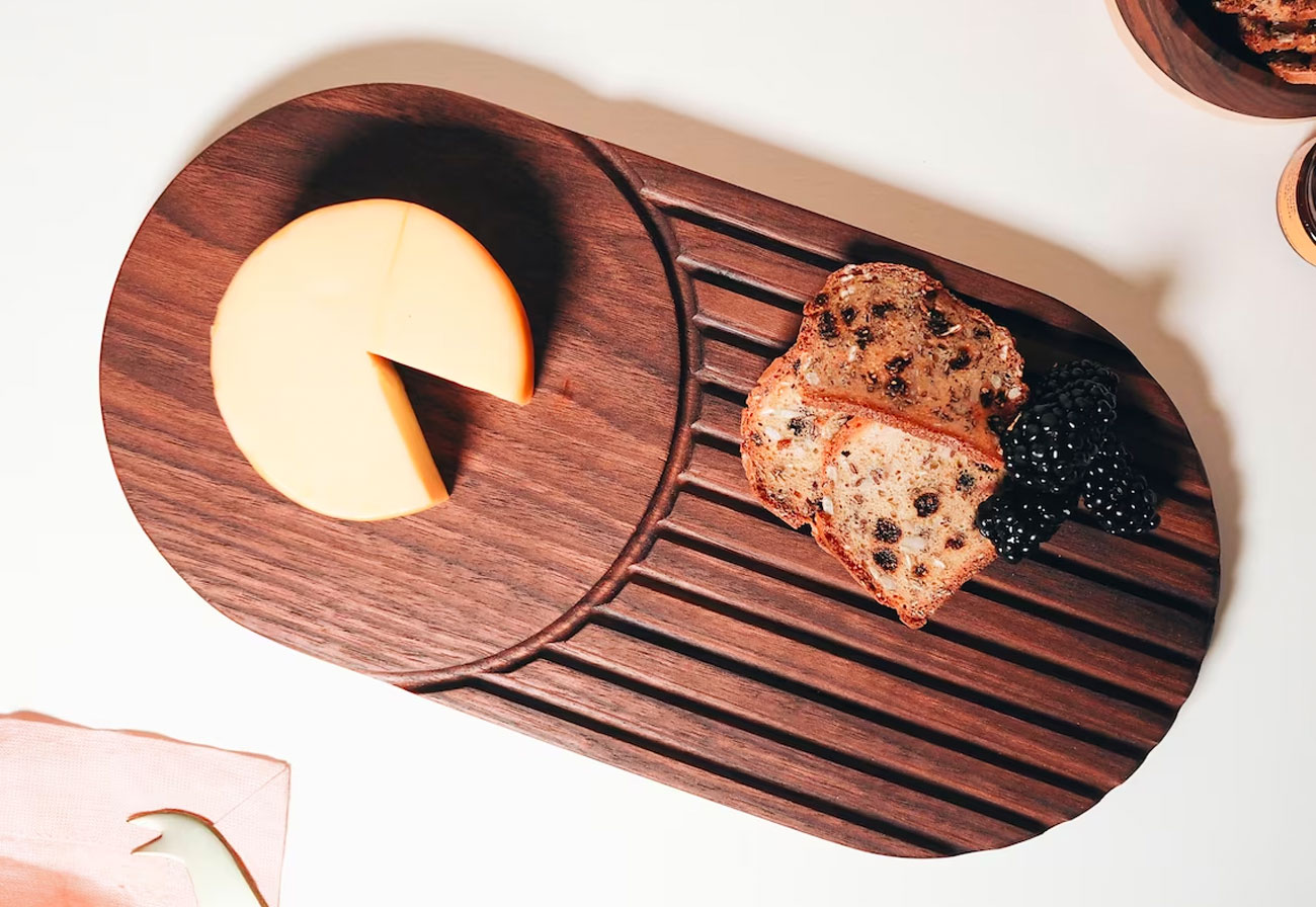 Wooden serving board with cheese, berries and crackers on it.