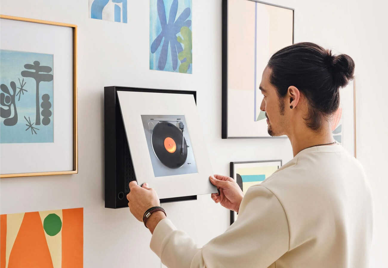 Man changing photo on wall-mounted Samsung Music Frame.