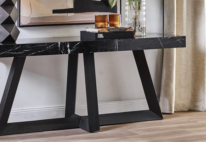 Black marble top console table on a wooden floor with books and a vase on top.