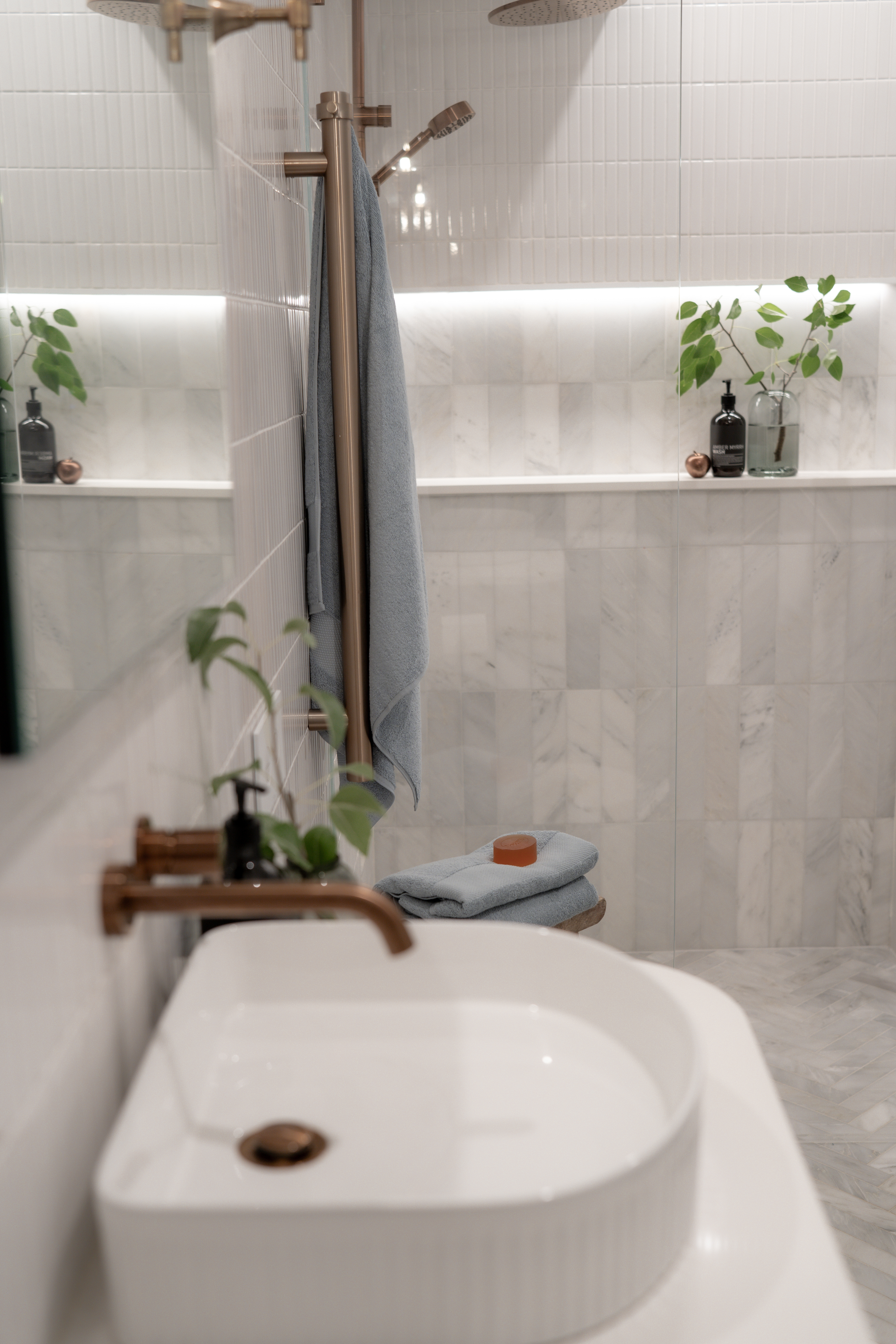 Narrow bathroom with shower niche and copper tapware.