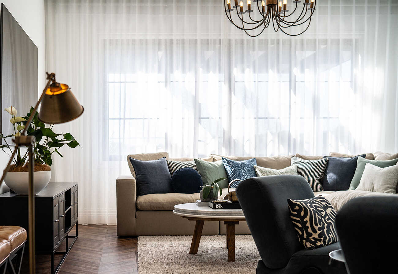 Living room with sheer curtains, a chandelier and herringbone wood floors. 