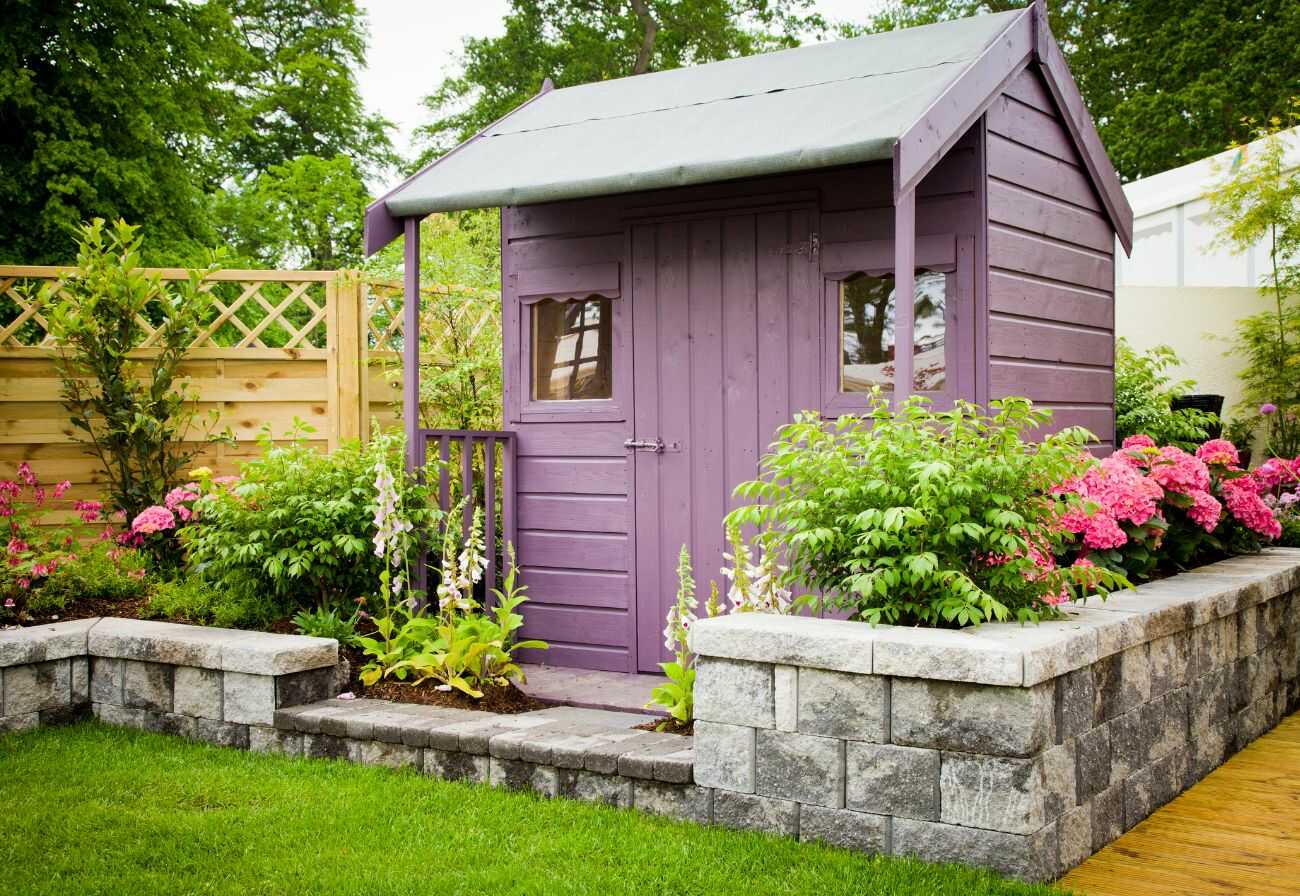 Purple garden shed with a short stone fence.