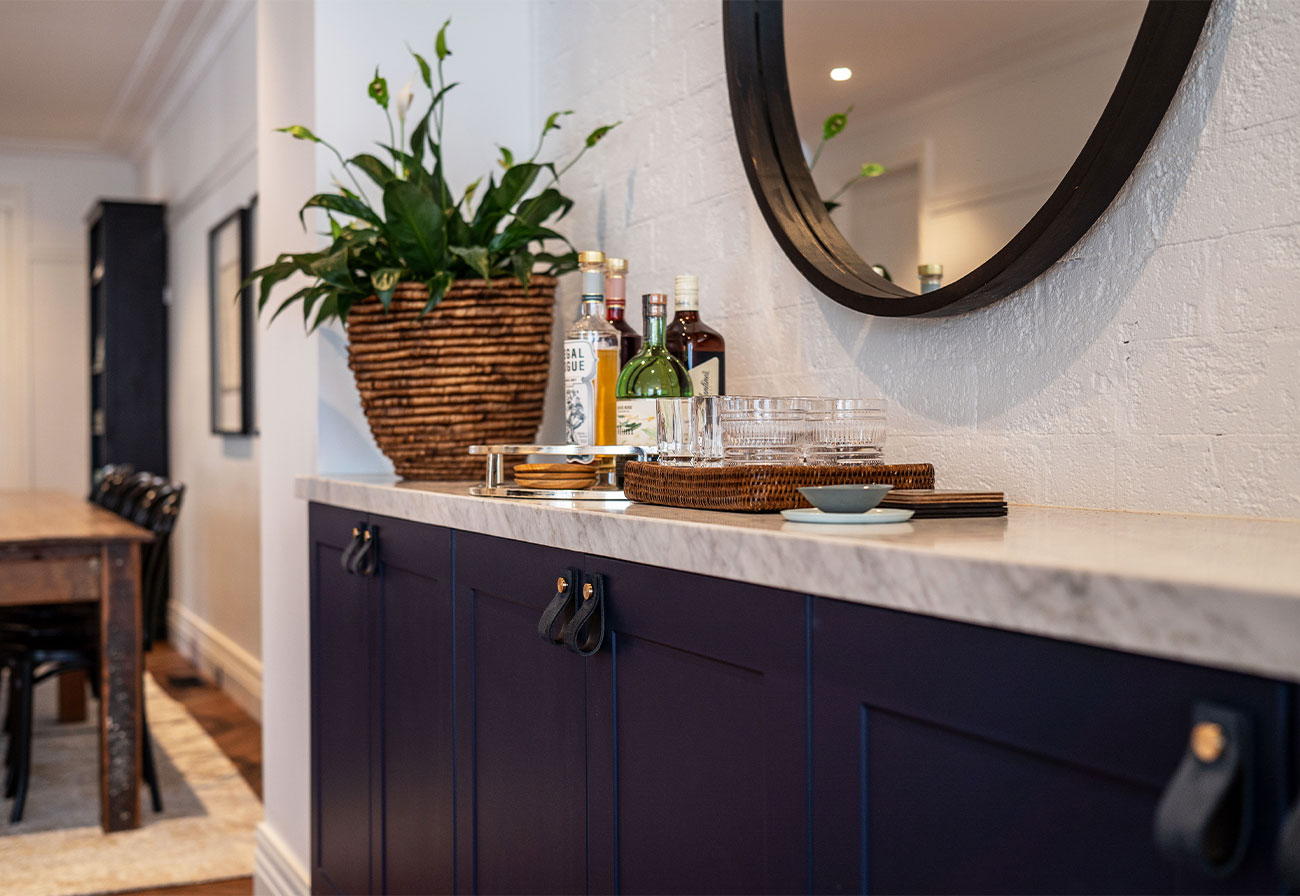 Sideboard with a marble benchtop, drinks and a plant.