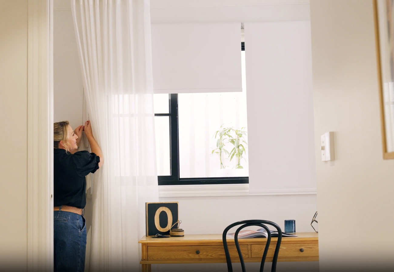 Adjusting white roller blinds above a desk. 