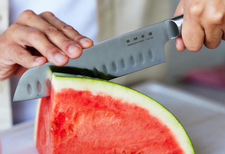 Person slicing watermelon with a SMEG knife.