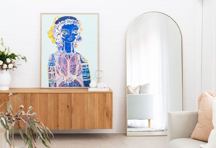 A gold-rimmed arch-shaped mirror next to a wooden buffet.