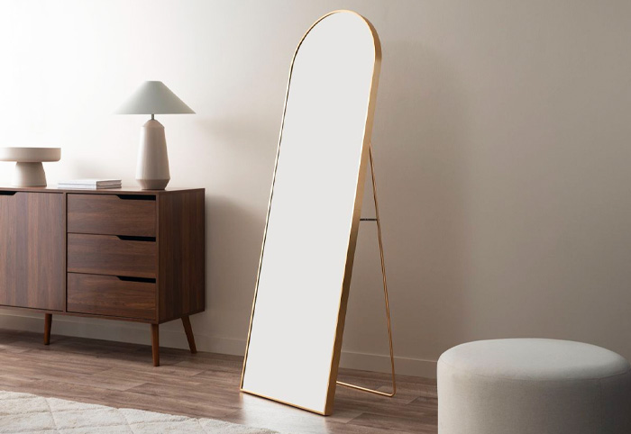 Freestanding gold mirror on a wooden floor next to a chestnut console table.