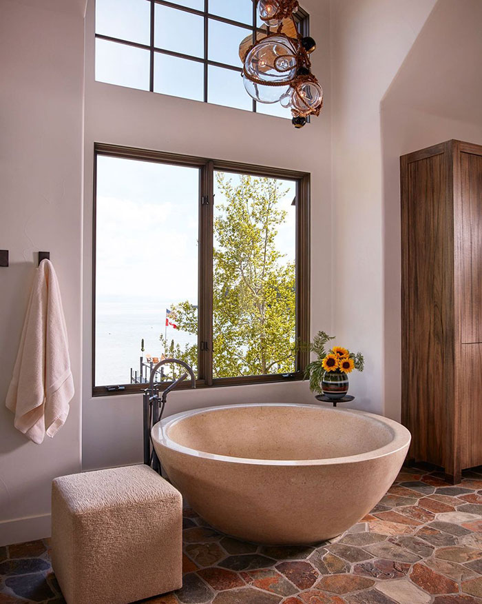 Round stone bathtub next to a large window.