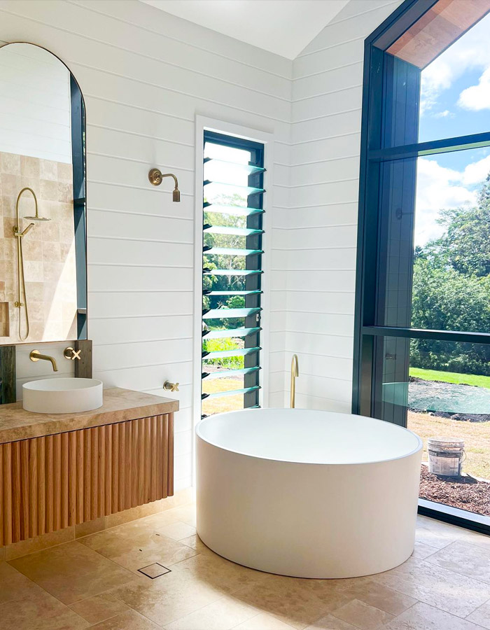 Renovated bathroom with white bath, gold taps and wooden vanity.