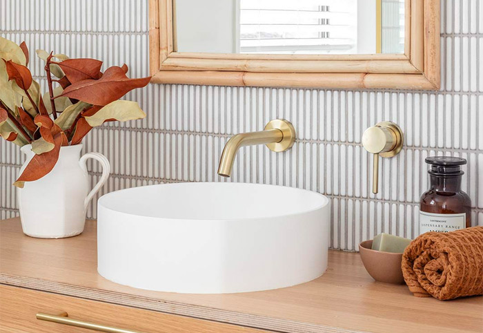 Brushed brass spout and mixer wall-mounted in a bathroom.