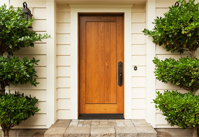 Cream house with a timber front door next to green trees.