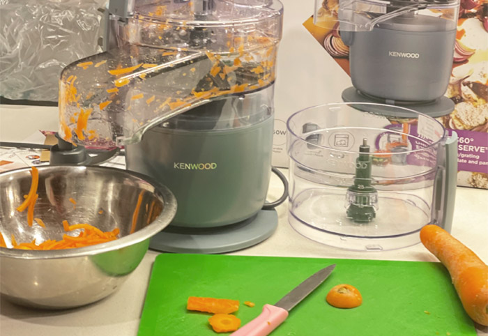 Kitchen bench with a food processor, green cutting board and knife on it. 