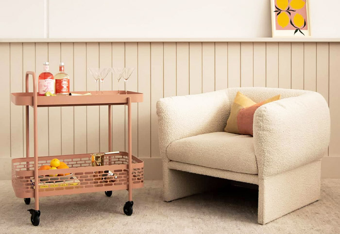 Gingerbread-coloured serving trolley next to a white armchair. 