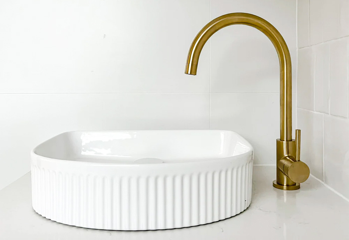 Yabby brushed brass kitchen mixer tapware with a white basin.