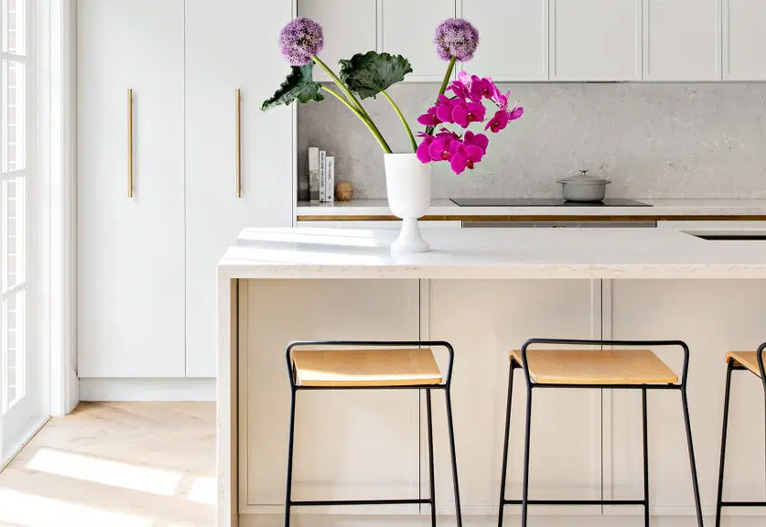 White kitchen bench with vibrant flowers on top.