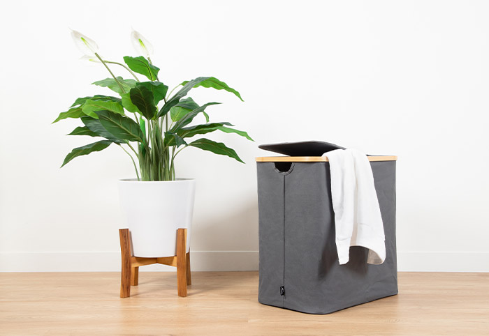 Grey laundry hamper on a hardwood floor next to a pot plant.