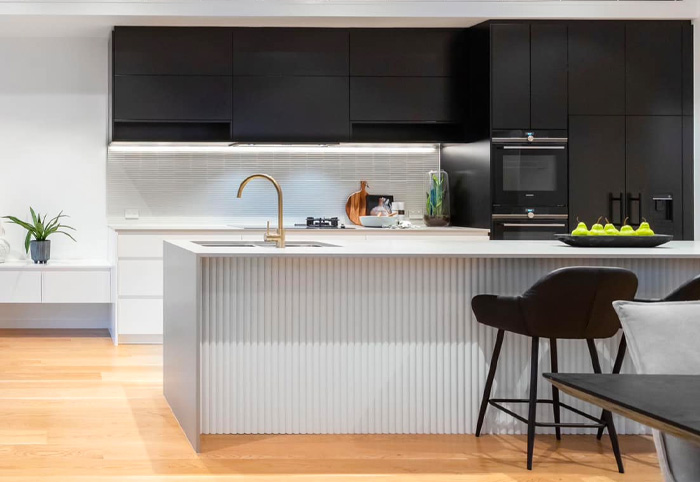 Kitchen with concrete-look island bench, gold tapware and black cabinets. 