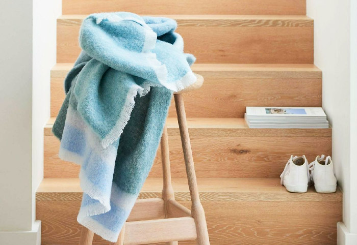 Blue St Albans luxury blanket on a stool at the bottom of a wooden staircase.