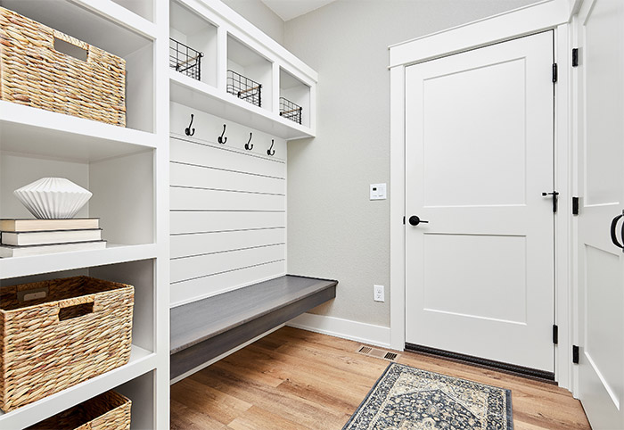 A white mud room with black hooks and wicker baskets.