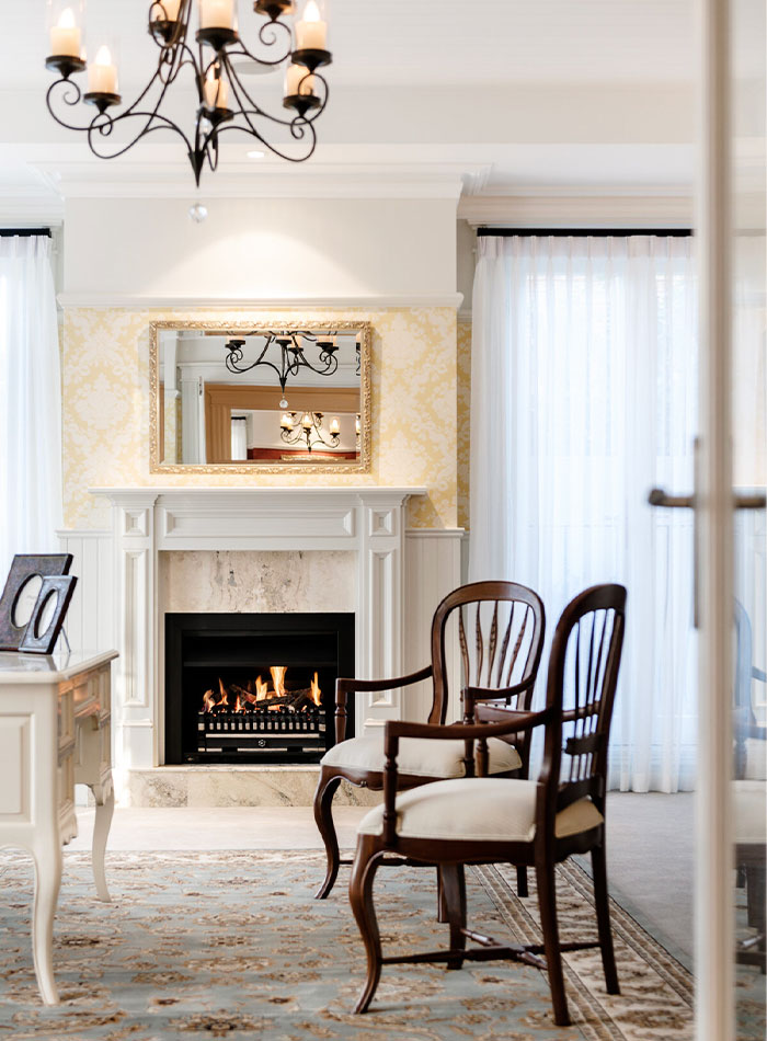 Vintage timber chairs with cabriole legs next to a fireplace in a living room.