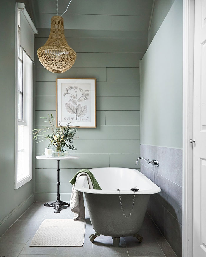 A muted green bathroom with a claw-foot bath tub. 