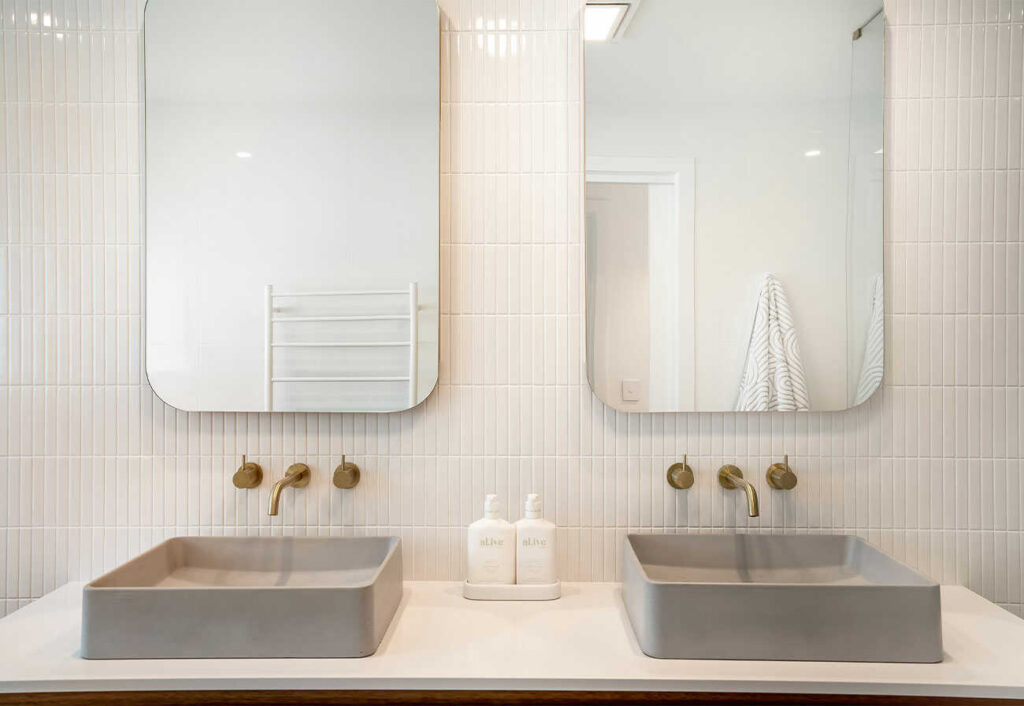 Bathroom vanity with concrete-look basins, brass tapware and curved mirrors.