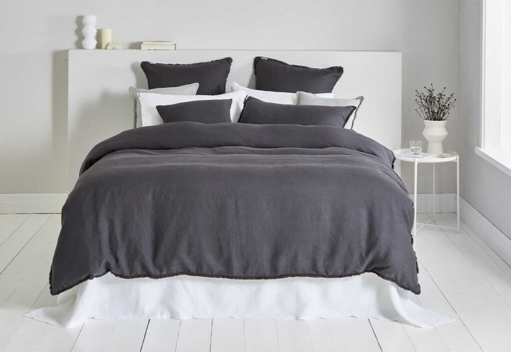 Bed with asphalt-coloured quilt cover in a white room. 