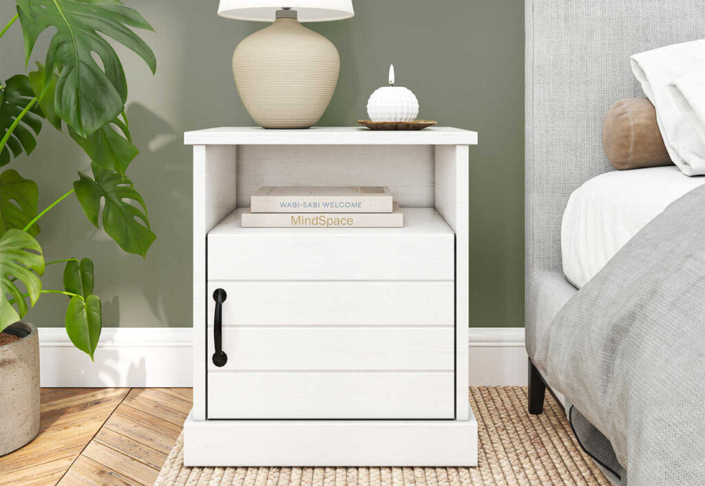 White coastal bedside table with two books, a beige reading lamp and a candle on top.