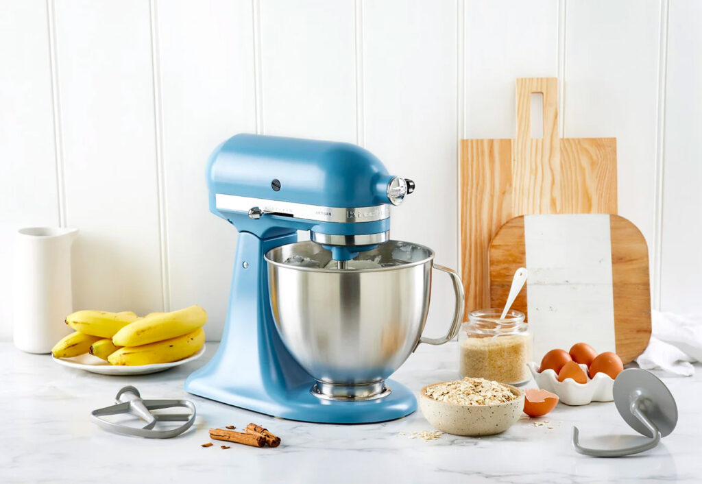 Kitchenaid Blue Velvet Stand Mixer on a white bench next to a plate of bananas and some baking ingredients.