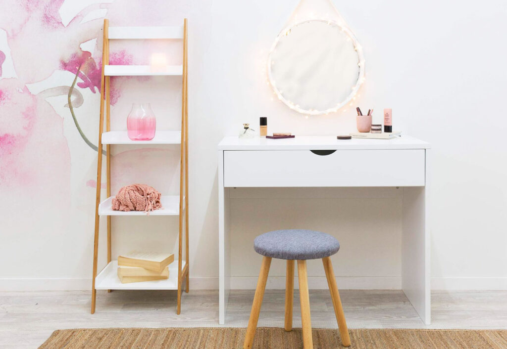 White make-up table shown under a round mirror and next to a ladder shelf.