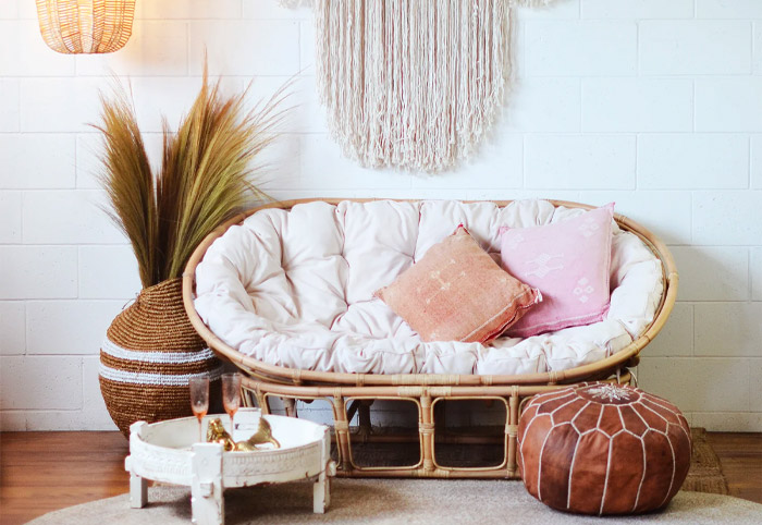 A double papasan chair against a white brick wall next to a Moroccan ottoman.