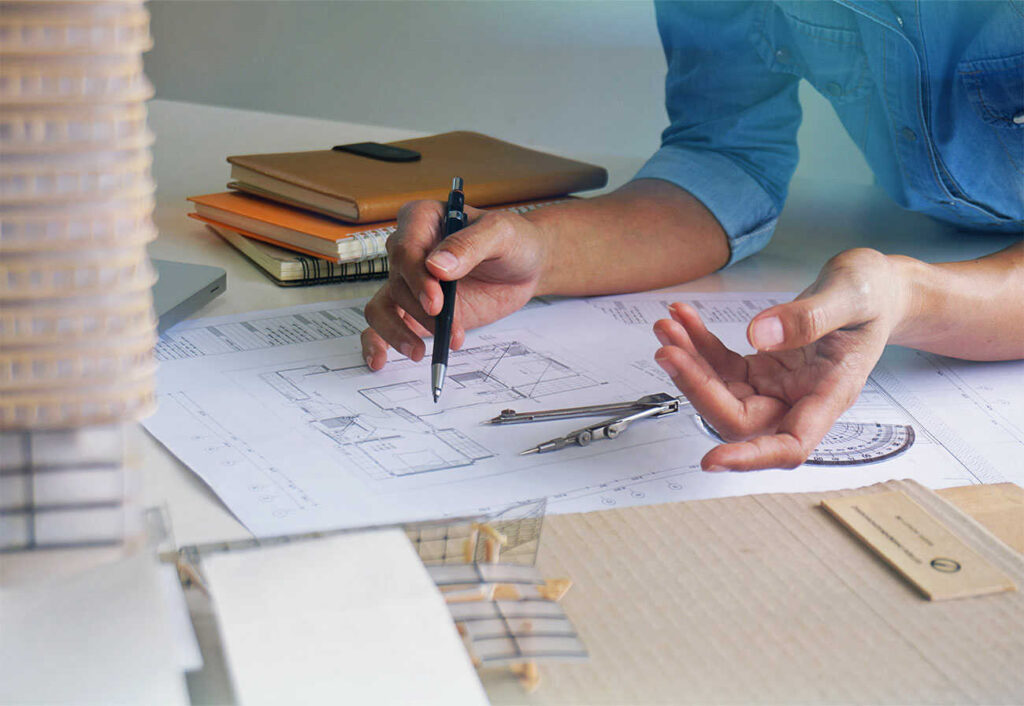 A person working over house plans holding a pen.