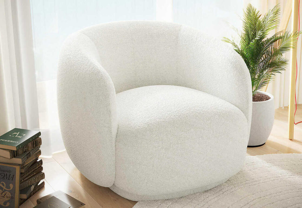 White cushioned boucle armchair in front of a window.