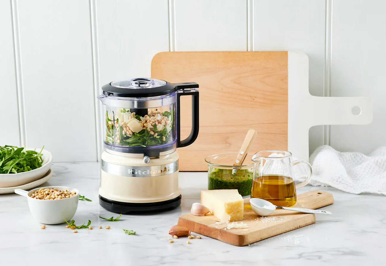 The Kitchenaid Mini Food Chopper on a white stone bench surrounded by cooking equipment and food.